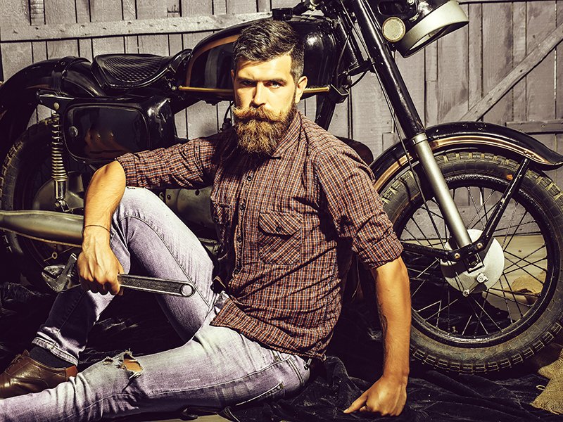 Hipster biker sitting against motorcycle